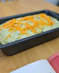 A golden brown loaf of green onion zucchini cheddar quick bread sliced on a wooden board