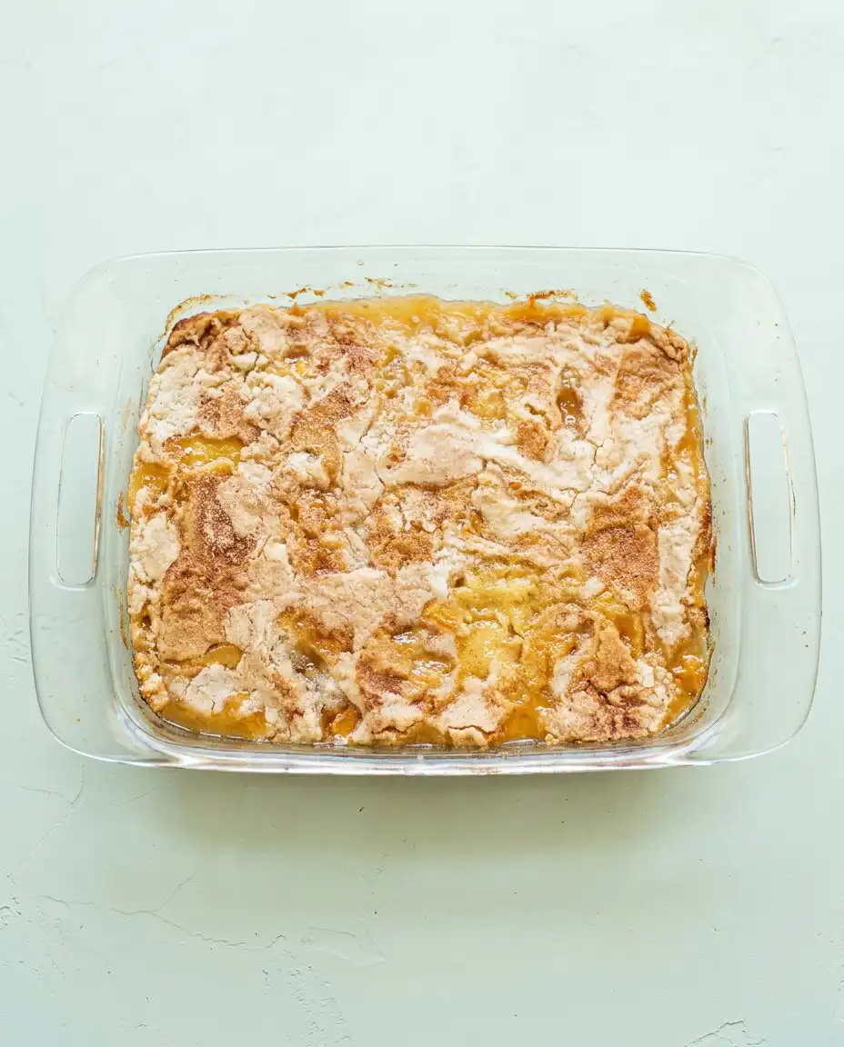 A warm serving of 3-Ingredient Peach Cobbler Dump Cake with a scoop of white cream.