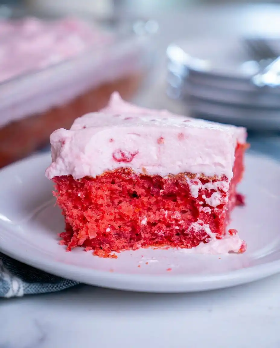 A square slice of pink raspberry cake with white fluff icing on a vintage floral china plate