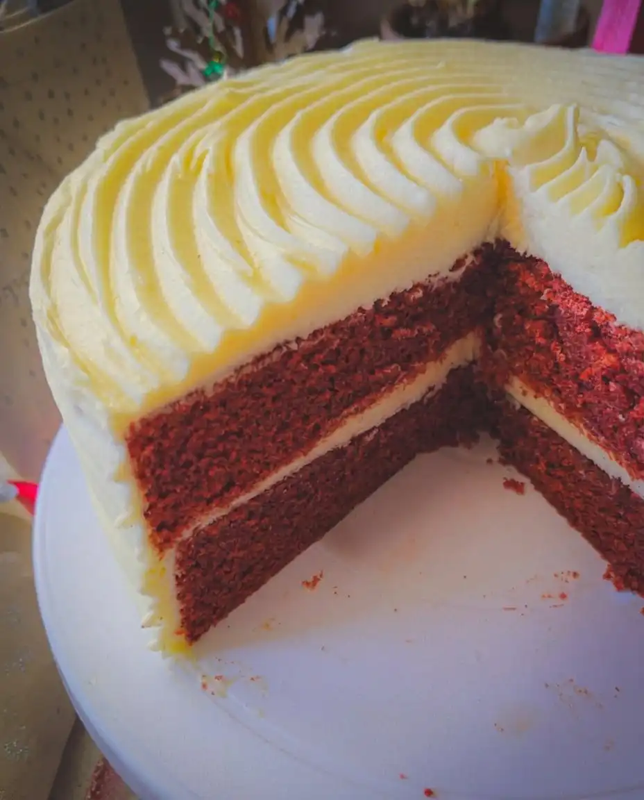 A single slice of red velvet cake with cream cheese frosting on a vintage floral china plate