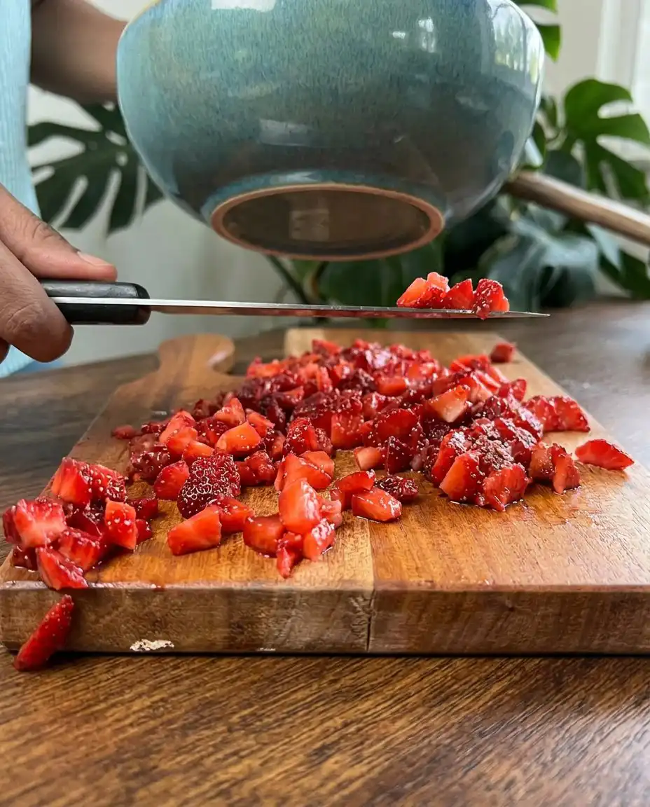A chef slicing fresh red strawberries for a Strawberry Vanilla Cake.