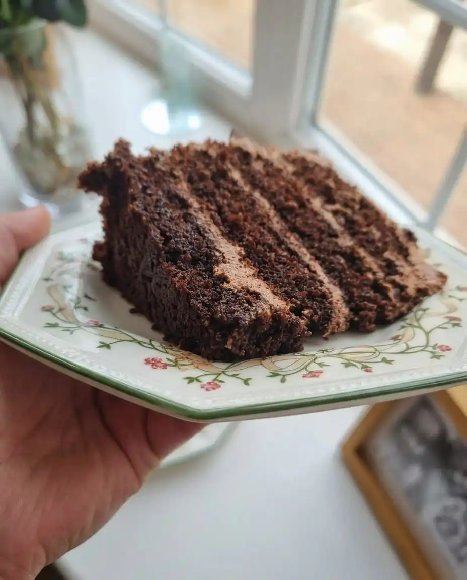 A chef smoothing thick chocolate ganache over cake layers