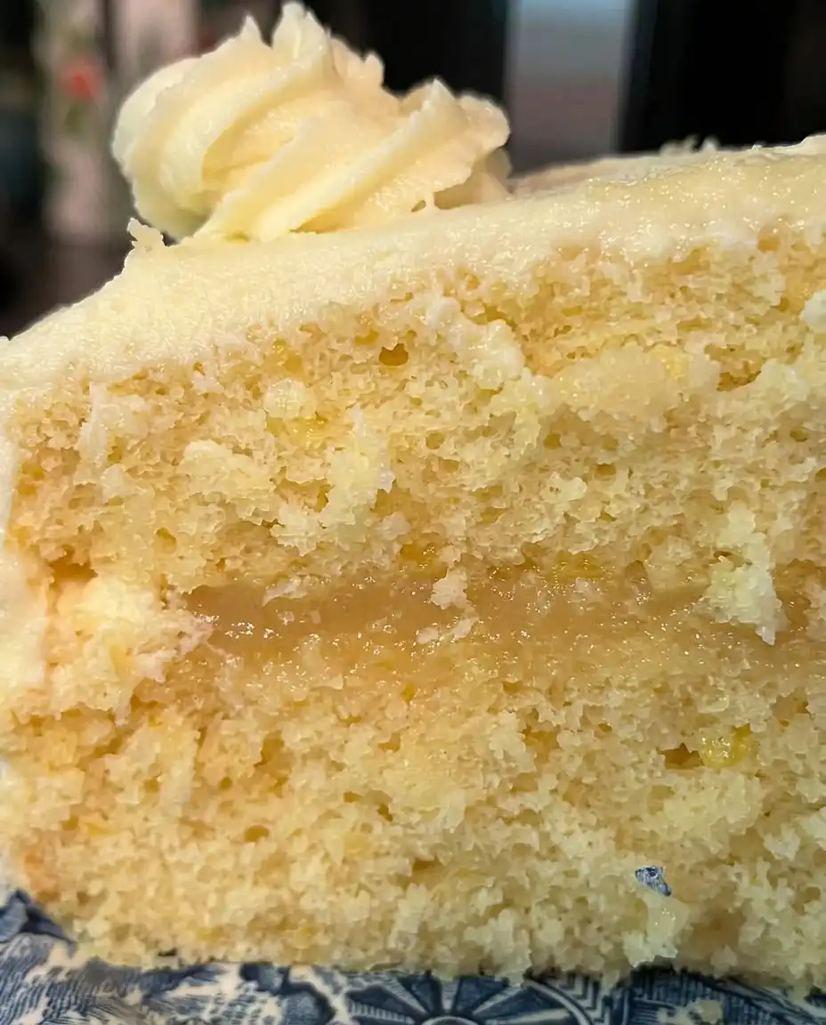 A hand using an offset spatula to spread lemon cream cheese frosting onto a yellow cake layer.
