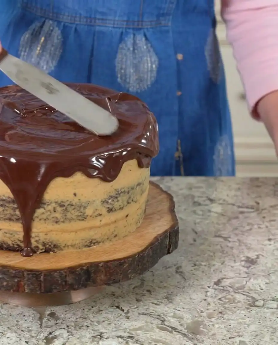 A spatula smoothing creamy peanut butter frosting onto a chocolate cake layer