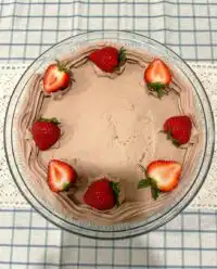 A tall strawberry chocolate cake with pink frosting and fresh strawberry halves on top