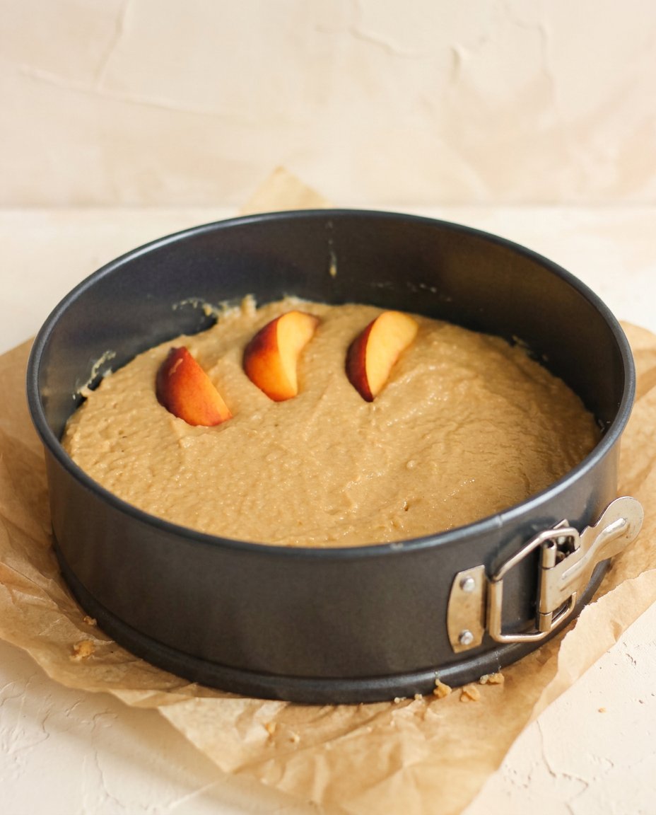 A hand using a spatula to swirl cinnamon peaches into Sour Cream Peach Coffee Cake batter.
