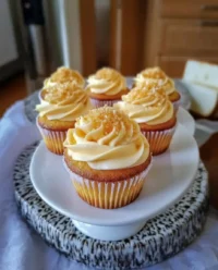 A tray of honey peach cream cheese cupcakes with fresh peach slices on a vintage lace tablecloth