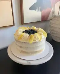 A three layer lemon blueberry cake on a vintage wooden table with a floral tablecloth