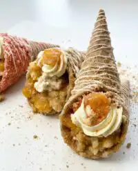 A peach cobbler cheesecake cone being held on a sunny porch