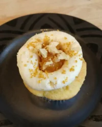 A single peach and honey cheesecake cupcake on a white lace doily with fresh peach slices.
