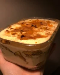 A beautiful serving of peach tiramisu in a vintage glass dish with fresh peach slices.