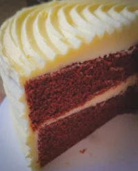 A three layer red velvet cake with white cream cheese frosting on a rustic wooden table