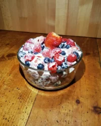 A clear glass bowl filled with fluffy Red, White & Blue Cheesecake Salad sitting on a vintage picnic blanket.
