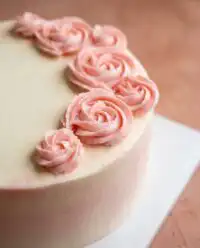 An elegant Rose Water Layer Cake decorated with pink rosettes and sparkling sugar.