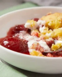 A golden brown strawberry cheesecake dump cake in a glass baking dish