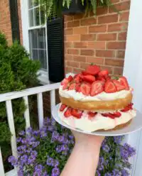 A vintage Strawberry ‘Shortcake’ Layer Cake on a white ceramic stand with fresh berries