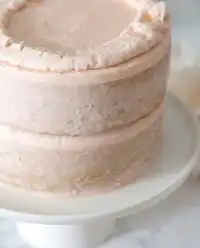 A vintage Two-Layer Smash Cake decorated with pink buttercream roses sits on a weathered wooden stool.
