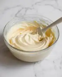 A glass bowl filled with fluffy white vanilla mousse cake filling with a vintage silver spoon