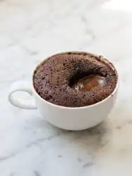 A freshly baked Chocolate Lava Mug Cake in a blue ceramic mug with a molten core oozing out.