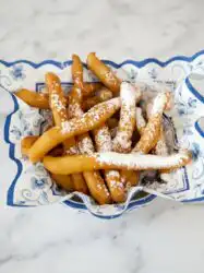 Freshly golden Cinnamon Sugar Funnel Cake Fries dusted with sweet cinnamon and sugar on a vintage plate