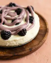 An elegant three layer Blackberry Vanilla Cake decorated with fresh blackberries and vanilla bean frosting on a ceramic stand.