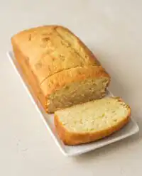 A classic Cream Cheese Pound Cake with a golden brown crust displayed on a white marble stand.