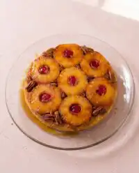 A golden brown Classic Pineapple Upside Down Cake resting on a wire rack with glazed pineapples.