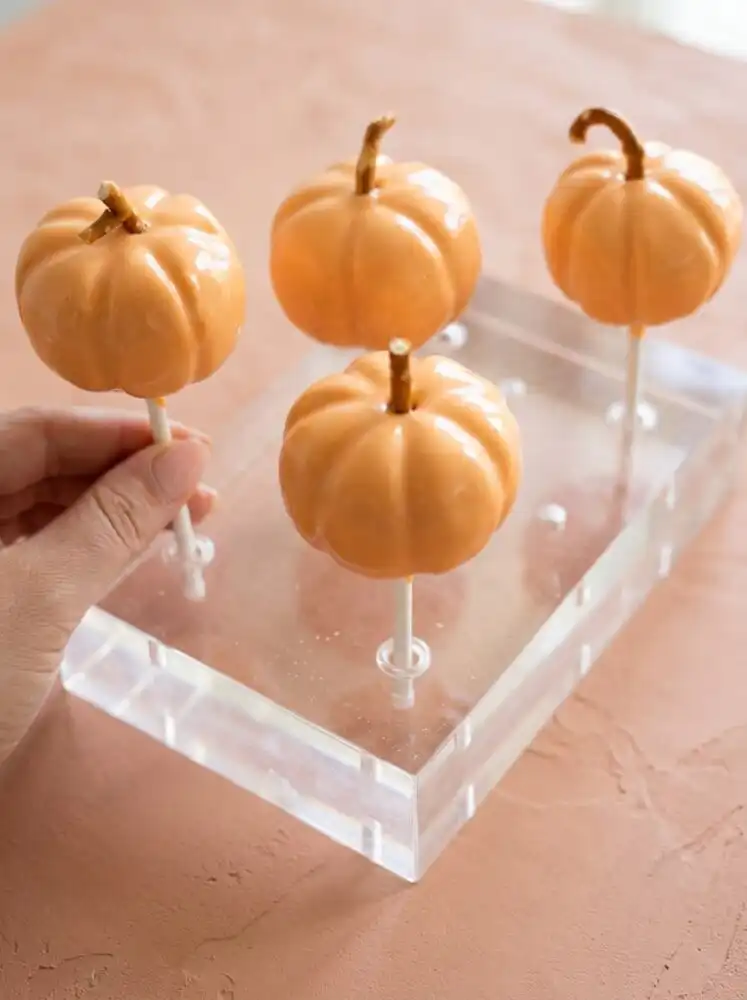 A vintage wooden stand displaying decorated Classic Pumpkin Cake Pops with chocolate chip stems.