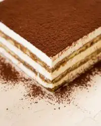 A beautifully sliced Classic Tiramisu Layer Cake sitting on a vintage glass dessert stand.