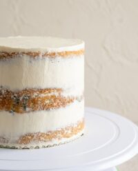A beautiful classic vanilla naked cake decorated with fresh raspberries on a white vintage cake stand.
