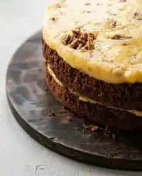 A decadent three layer German Chocolate Cake on a white ceramic stand with rich coconut pecan frosting.