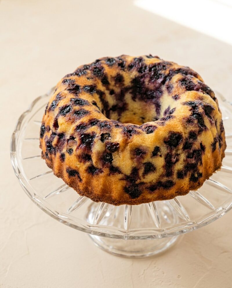 Home - Cake Half - Small Batch Baking & Cupcakes 5 A perfect golden Lemon Blueberry Bundt Cake with Lemon Glaze sitting on a rustic wooden stand.