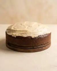 A rustic Marzipan Carrot Topped Cake resting on a vintage glass stand decorated with small marzipan carrots.
