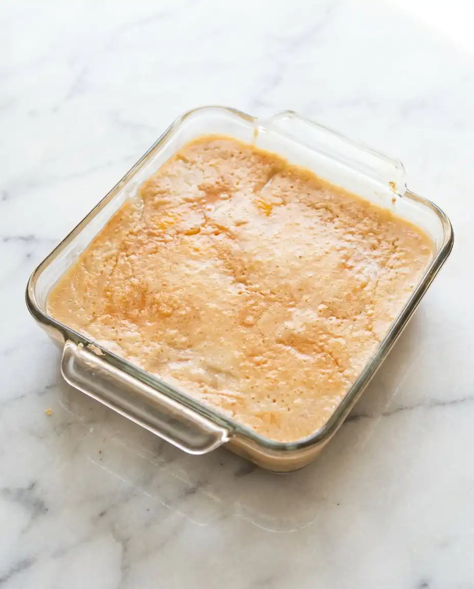 A plated serving of peach dump cake with frozen peaches topped with a melting scoop of vanilla ice cream.