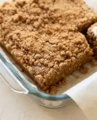 A golden Pumpkin Streusel Coffee Cake topped with a rustic brown sugar crumble and sliced pecans in a baking pan.