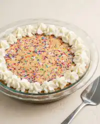 A beautifully decorated Rainbow Sprinkle Cookie Cake with a piped vanilla buttercream border.