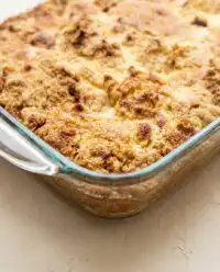 A close up photo of a slice of pumpkin dump cake served on a elegant white plate with autumn decorations.