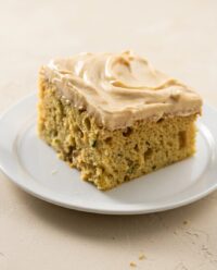 A close up of a sliced zucchini cake with cinnamon and nutmeg topped with cream cheese icing.