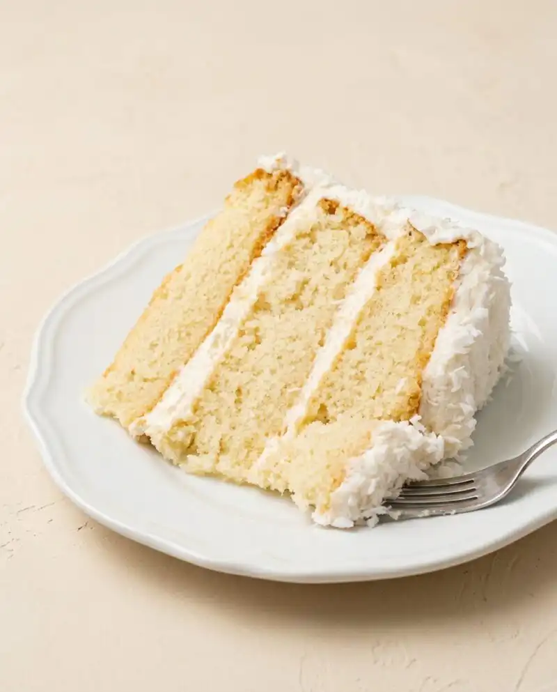Slices of Three-Layer Coconut Cream Cake displayed on a vintage glass cake stand.