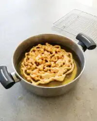 A golden crispy 3-Ingredient Funnel Cake dusted with a heavy layer of powdered sugar on a vintage plate.