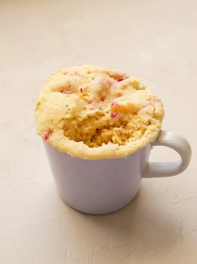 Home - Cake Half - Small Batch Baking & Cupcakes 4 A warm 1-Minute Vanilla Mug Cake served inside a vintage ceramic cup on a rustic wood surface