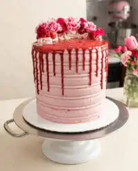 A beautiful White Chocolate Raspberry Anniversary Cake decorated with fresh raspberries on a vintage pedestal plate.